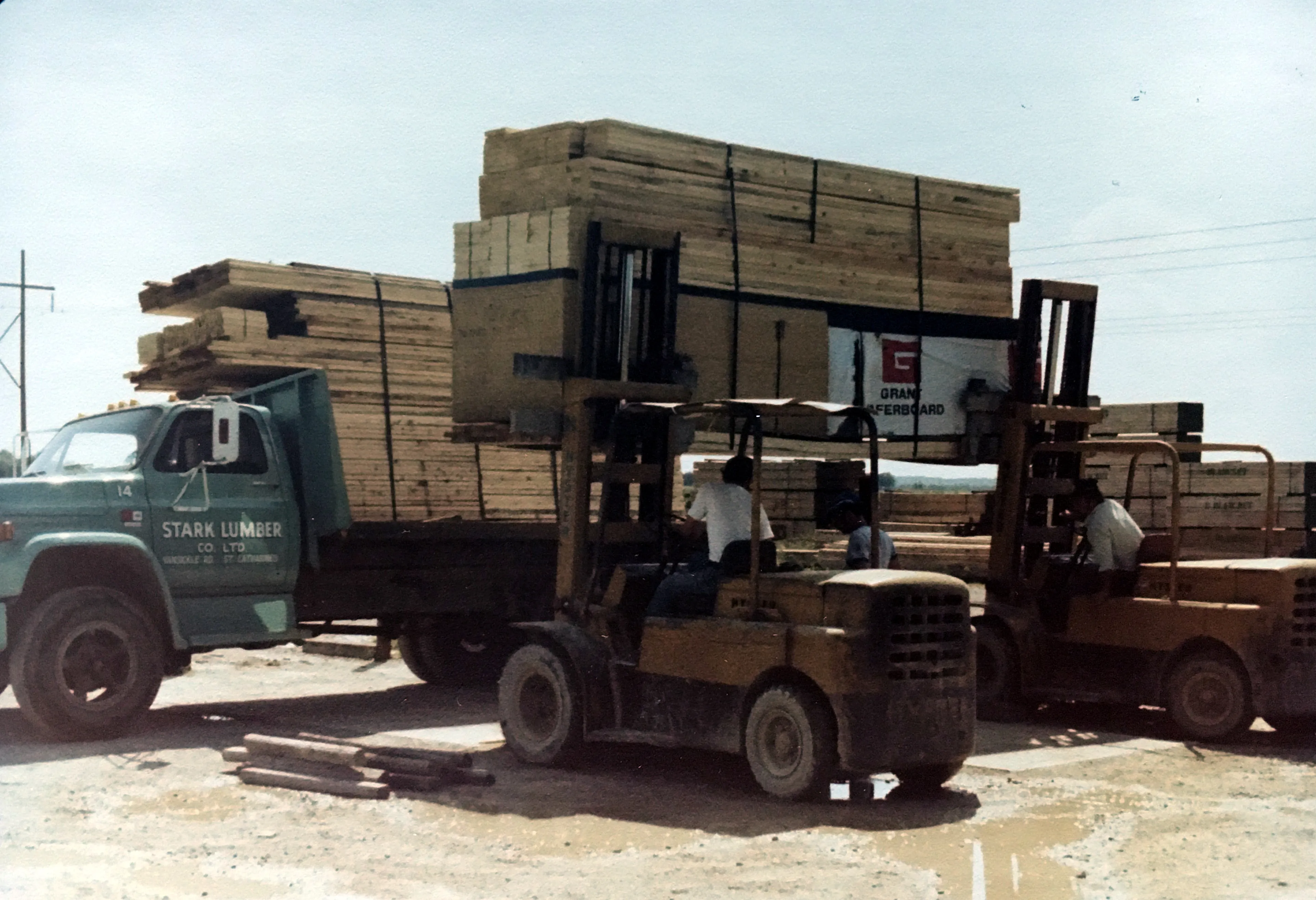 Two forklifts loading bundles of lumber onto a green Stark Lumber truck in the 1980s